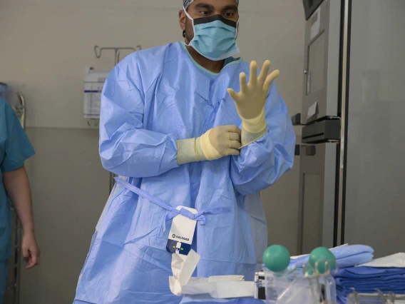 Health care worker in mask and surgical gown putting on a glove