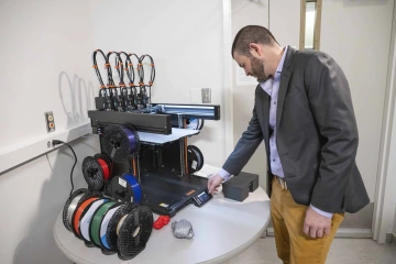 A man in a sports coat checks the activity of a 3D printer