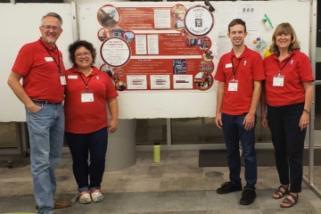 Four people stand in front of a poster with information about the Health Connectors program