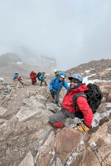 Six people in parkas and climbing gear climb up Aconcagua with clouds in the background.